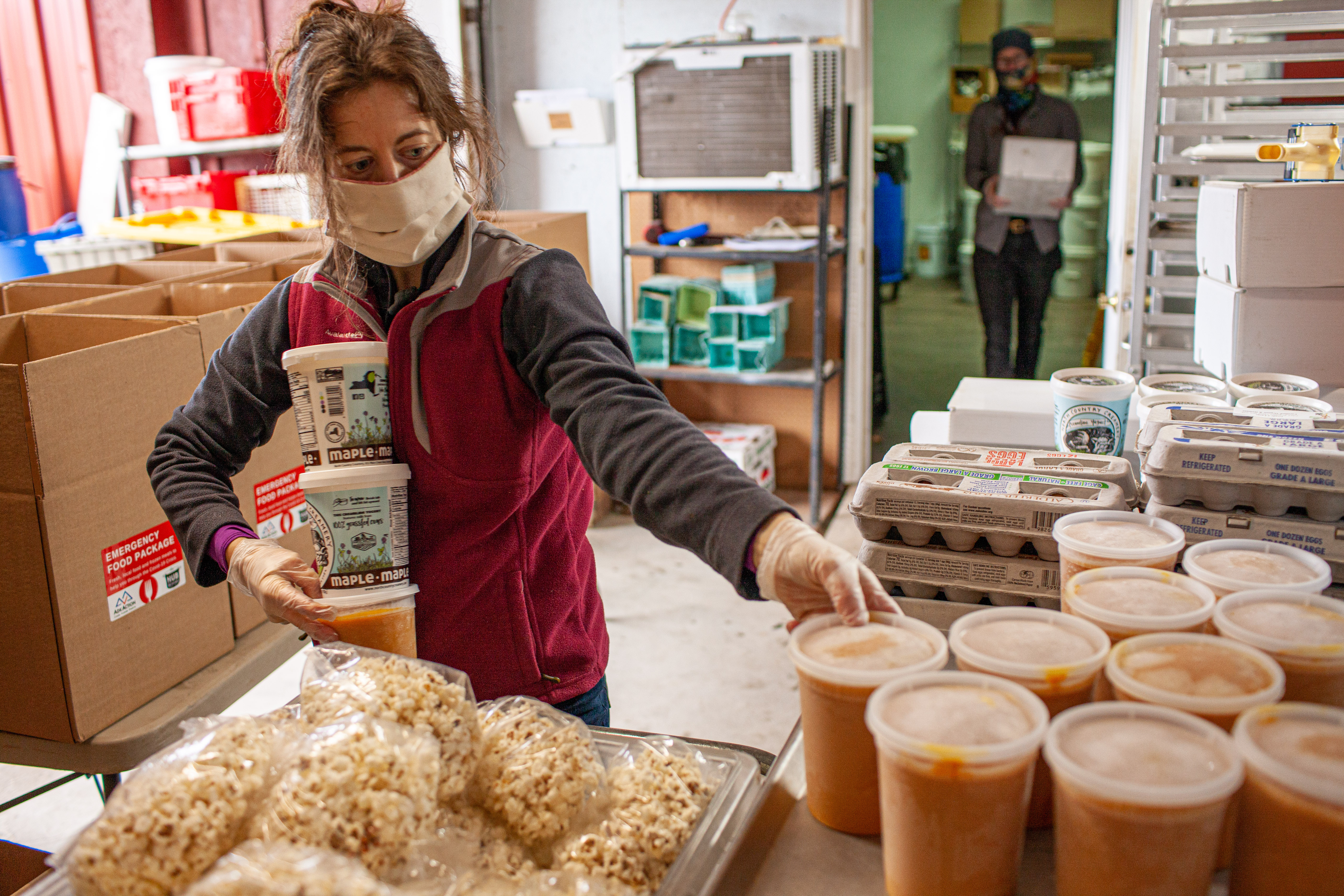 A woman wearing a mask packs emergency food boxes.