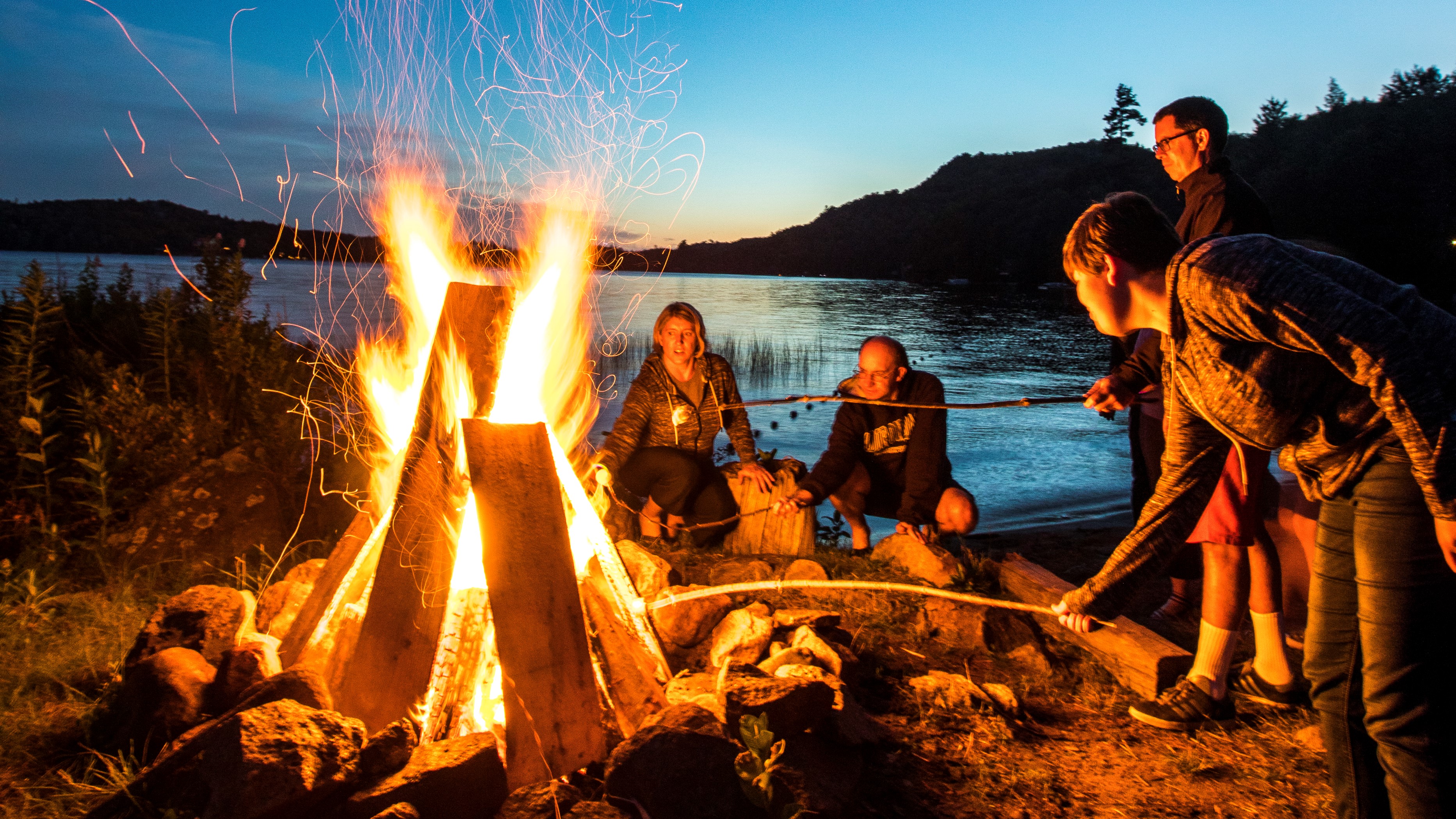 Roasting marshmallows around a fire near a lake