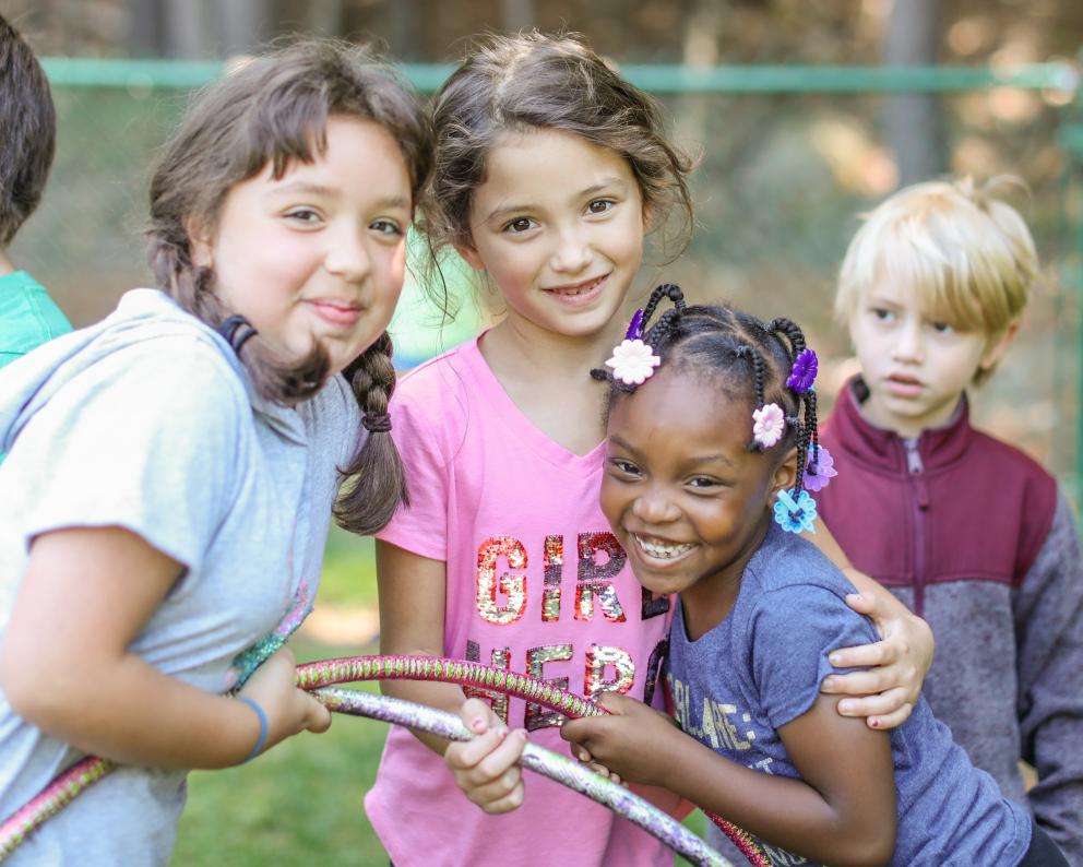 Smiling kids gather with a hoola hoop.