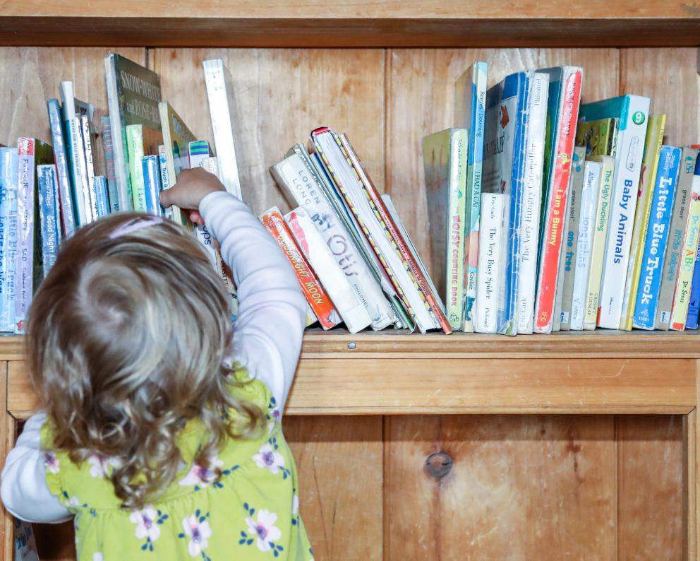 Young girl reaching for book at Lakeside School in Essex, NY