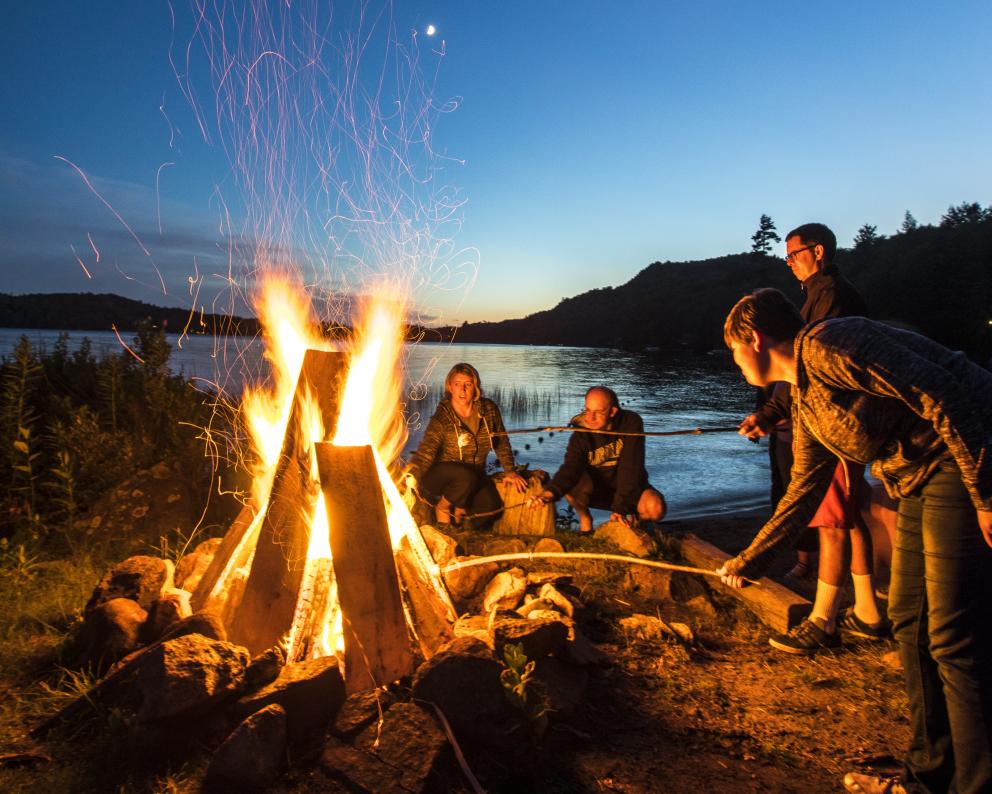 Roasting marshmallows around a fire near a lake