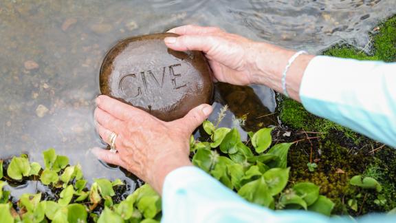Hands holding rock engraved with the word give in water
